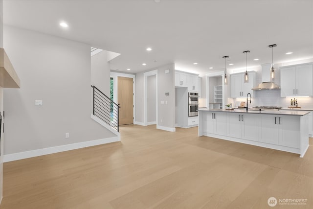 kitchen with tasteful backsplash, wall chimney exhaust hood, light wood-style flooring, stainless steel appliances, and a sink