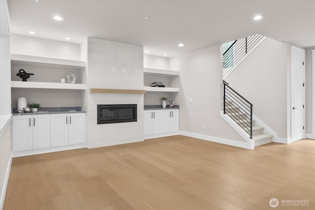 unfurnished living room with light wood-style floors, recessed lighting, a large fireplace, and built in features