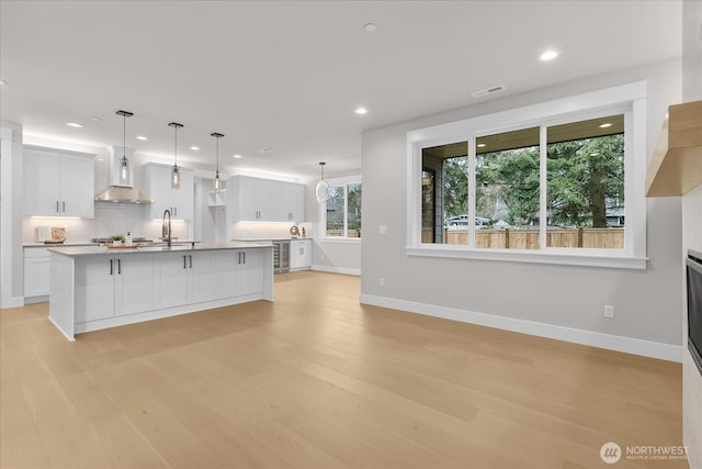 kitchen featuring tasteful backsplash, light wood-type flooring, visible vents, and wall chimney range hood