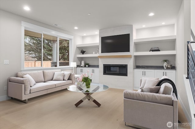 living room with recessed lighting, visible vents, built in features, and a glass covered fireplace