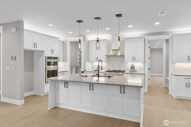 kitchen featuring stainless steel appliances, white cabinetry, light wood-style flooring, and wall chimney exhaust hood