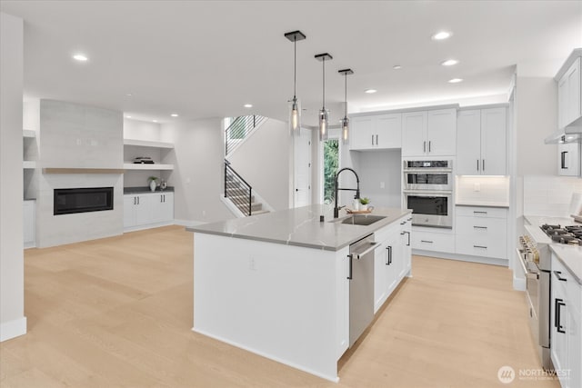 kitchen featuring pendant lighting, a fireplace, light wood-style flooring, appliances with stainless steel finishes, and a sink