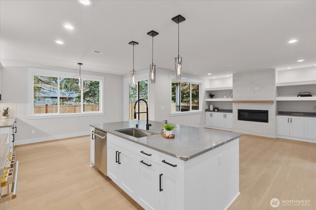 kitchen featuring light wood finished floors, stainless steel dishwasher, a sink, and a kitchen island with sink