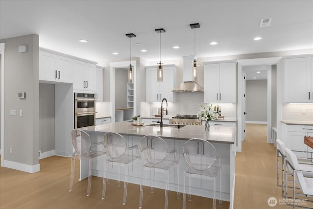 kitchen featuring wall chimney exhaust hood, stainless steel appliances, white cabinetry, and a kitchen breakfast bar