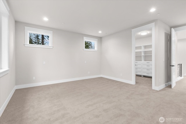 unfurnished bedroom with baseboards, recessed lighting, a walk in closet, and light colored carpet