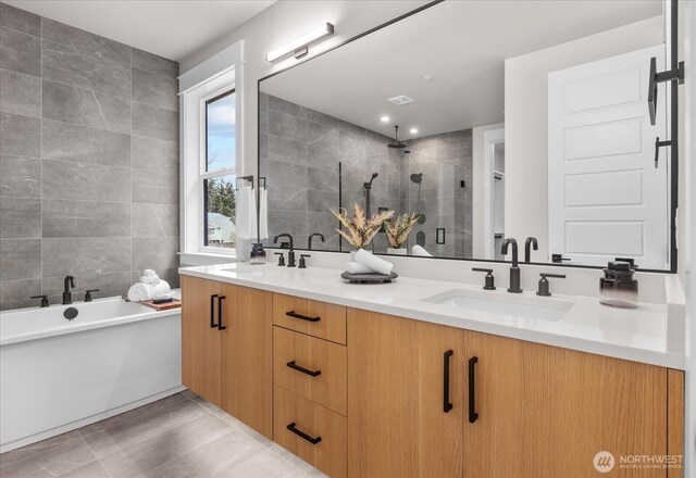 full bathroom featuring double vanity, a stall shower, a sink, and tile walls