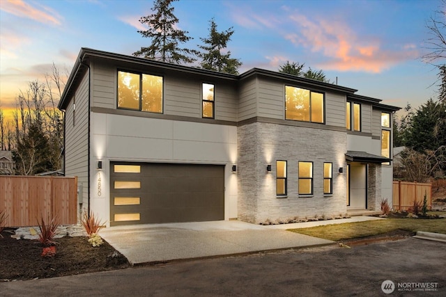 contemporary house with concrete driveway, stone siding, an attached garage, and fence