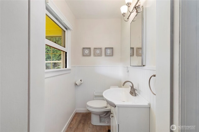 half bath featuring a wainscoted wall, toilet, an inviting chandelier, wood finished floors, and vanity