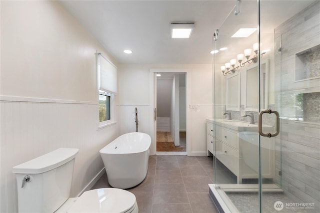 bathroom with a freestanding tub, toilet, a stall shower, and wainscoting