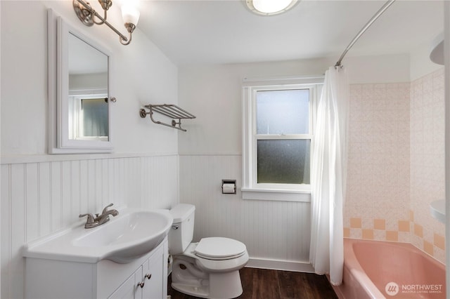 bathroom featuring a wainscoted wall, toilet, shower / tub combo with curtain, wood finished floors, and vanity