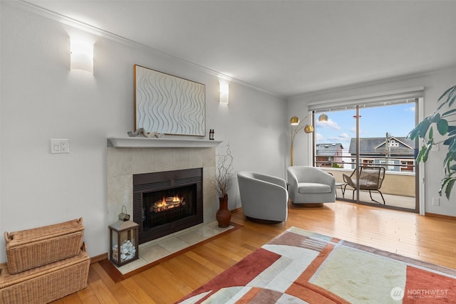 living area with ornamental molding, hardwood / wood-style floors, a tile fireplace, and baseboards