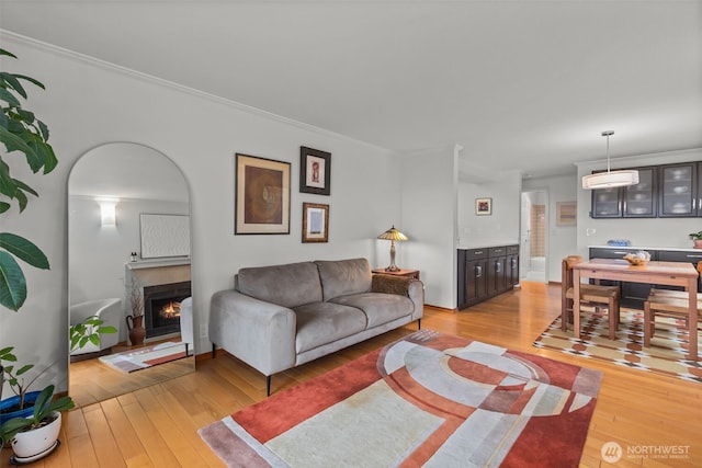 living area featuring arched walkways, crown molding, light wood finished floors, an AC wall unit, and a warm lit fireplace