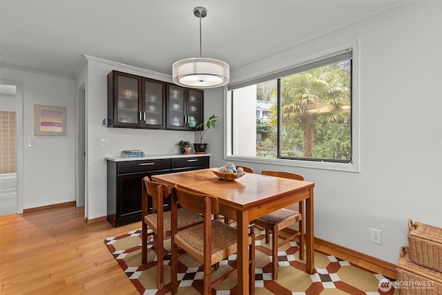 dining area with light wood-style floors, baseboards, and crown molding