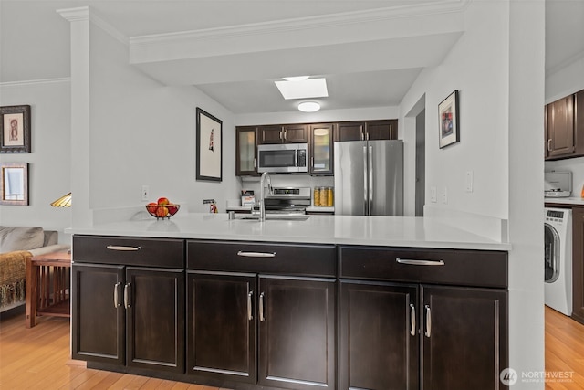 kitchen featuring washer / dryer, light wood-style flooring, stainless steel appliances, light countertops, and a sink