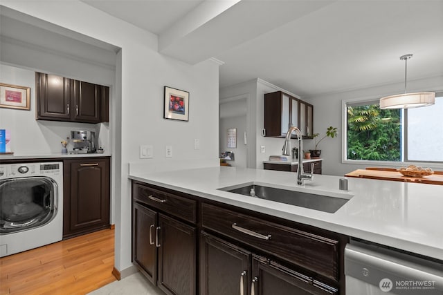 kitchen with light countertops, stainless steel dishwasher, a sink, dark brown cabinets, and washer / dryer