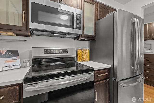 kitchen with stainless steel appliances, light wood-type flooring, light countertops, and dark brown cabinetry