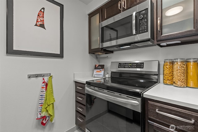 kitchen featuring appliances with stainless steel finishes, light countertops, glass insert cabinets, and dark brown cabinets