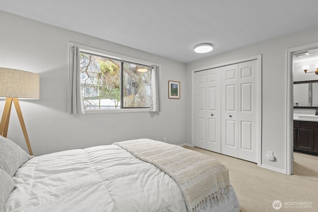 bedroom with a closet, light carpet, connected bathroom, a sink, and baseboards