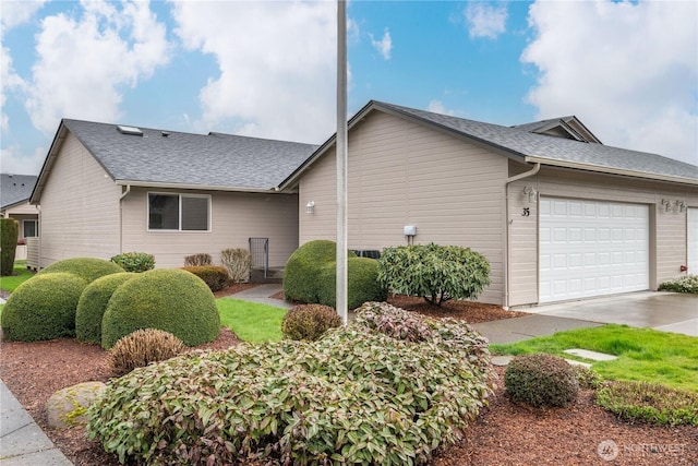 view of side of property with concrete driveway, roof with shingles, and an attached garage