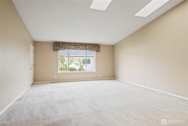 unfurnished room with lofted ceiling with skylight, carpet flooring, visible vents, and baseboards