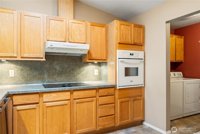 kitchen with white oven, black electric cooktop, under cabinet range hood, washing machine and dryer, and backsplash