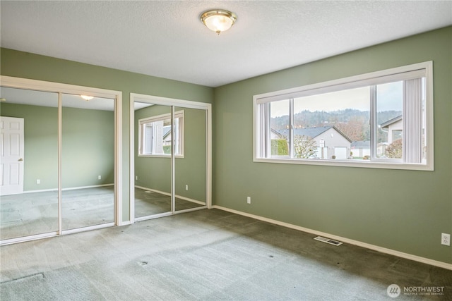 unfurnished bedroom with baseboards, multiple windows, visible vents, and multiple closets