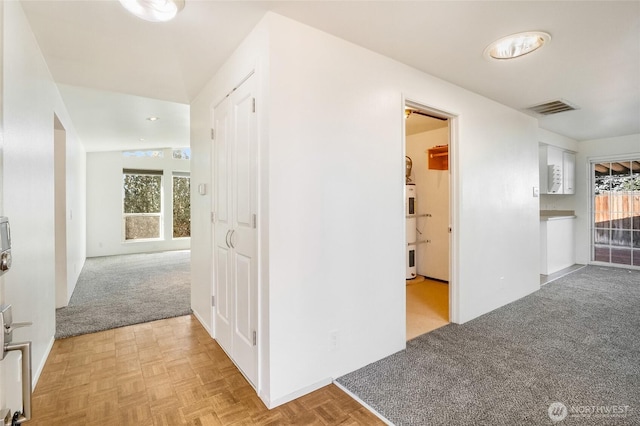 hallway featuring electric water heater, light colored carpet, visible vents, and a healthy amount of sunlight