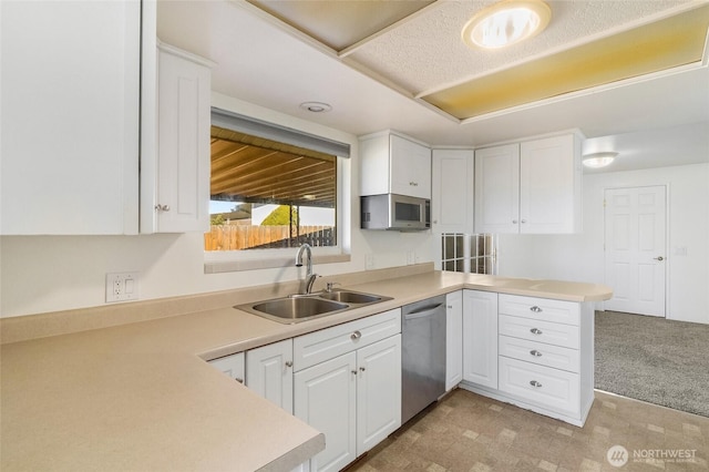 kitchen featuring white cabinets, a peninsula, stainless steel appliances, light countertops, and a sink