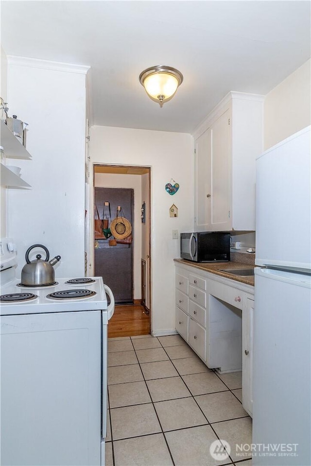 kitchen with white appliances, white cabinets, a sink, and light tile patterned flooring