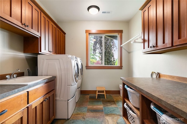 washroom with a sink, visible vents, cabinet space, stone finish floor, and washing machine and clothes dryer