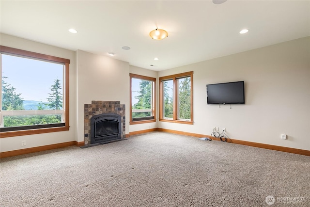 unfurnished living room featuring a tiled fireplace, carpet, a wealth of natural light, and baseboards