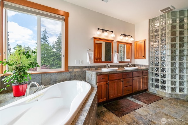 bathroom with double vanity, tiled bath, a sink, and stone finish flooring