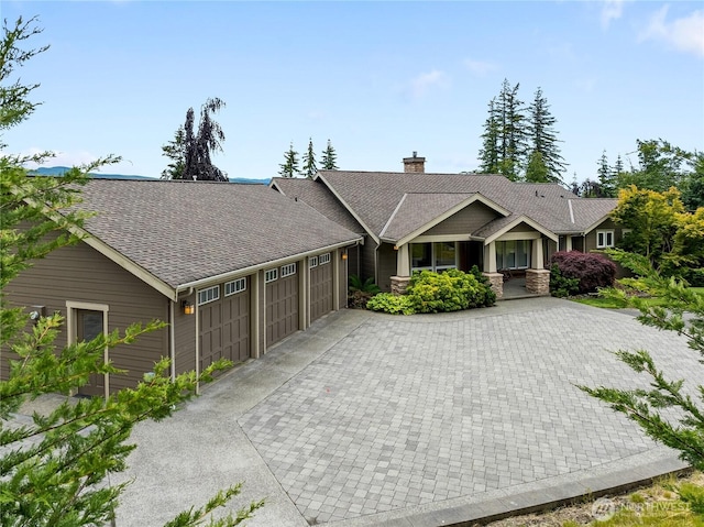 view of front of house with a chimney, roof with shingles, decorative driveway, and an attached garage