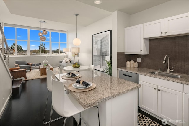 kitchen featuring light stone counters, a sink, dishwasher, white cabinetry, and backsplash