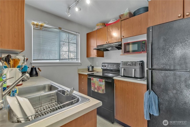 kitchen featuring brown cabinets, light countertops, a sink, under cabinet range hood, and black appliances