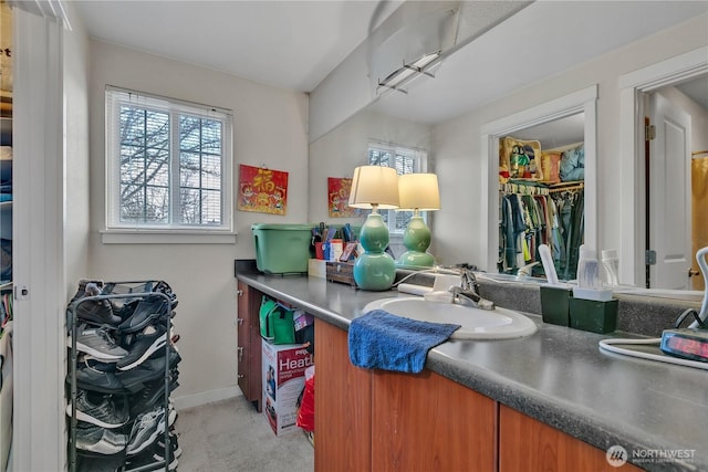 bathroom with baseboards, a walk in closet, and vanity