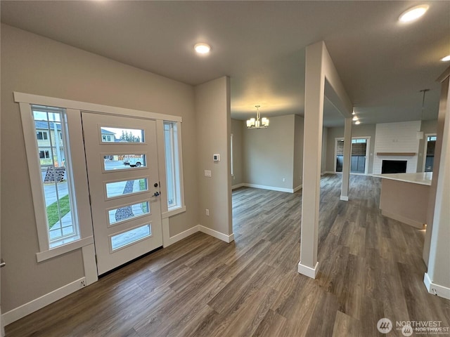 entrance foyer featuring a fireplace, baseboards, a chandelier, and dark wood-style flooring