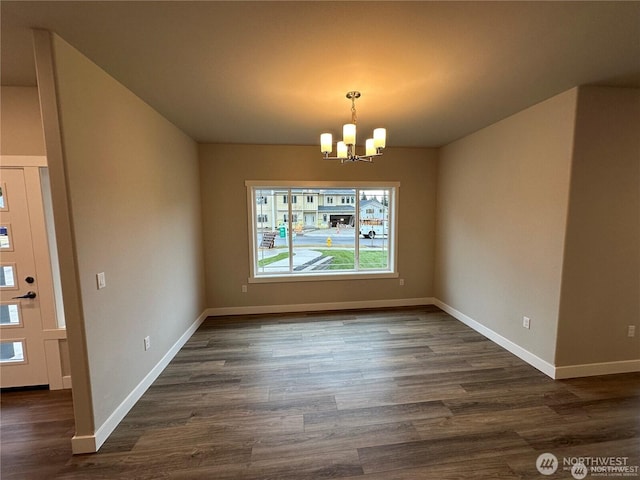 unfurnished dining area with dark wood-style floors, a notable chandelier, and baseboards