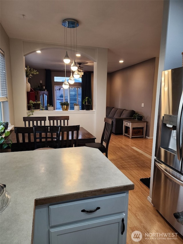 kitchen featuring pendant lighting, arched walkways, stainless steel fridge, and light wood-style floors