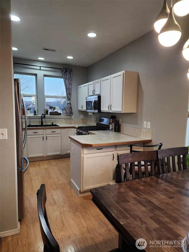 kitchen featuring stainless steel appliances, visible vents, white cabinetry, light wood-type flooring, and a peninsula