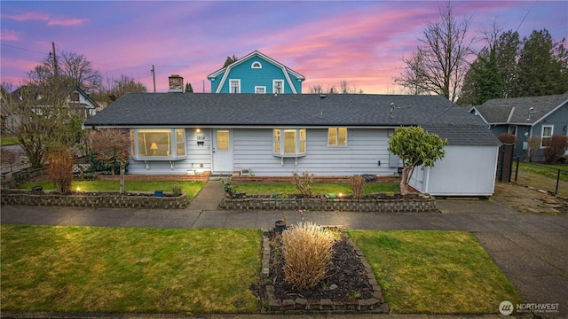 view of front of house featuring a storage shed, roof with shingles, a front lawn, and an outdoor structure