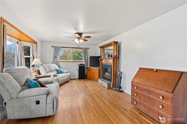 living room with a glass covered fireplace, baseboards, ceiling fan, and light wood finished floors