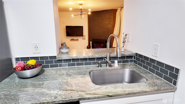 kitchen featuring a fireplace, light stone counters, backsplash, and a sink