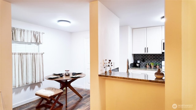 kitchen with dark wood-style flooring, tasteful backsplash, white cabinetry, dark stone countertops, and baseboards