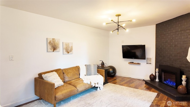 living room with a brick fireplace, a notable chandelier, baseboards, and wood finished floors