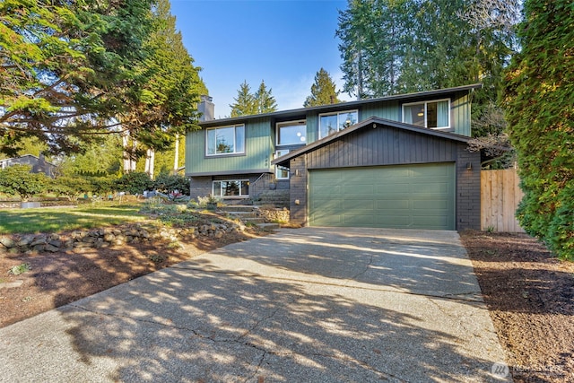 bi-level home featuring brick siding, concrete driveway, a chimney, and fence