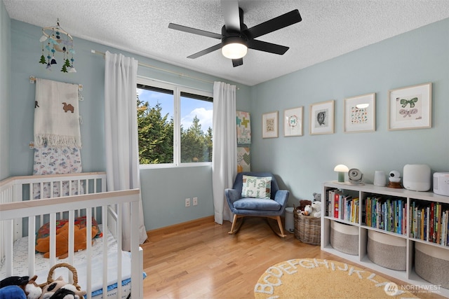 bedroom with wood finished floors, baseboards, ceiling fan, a nursery area, and a textured ceiling