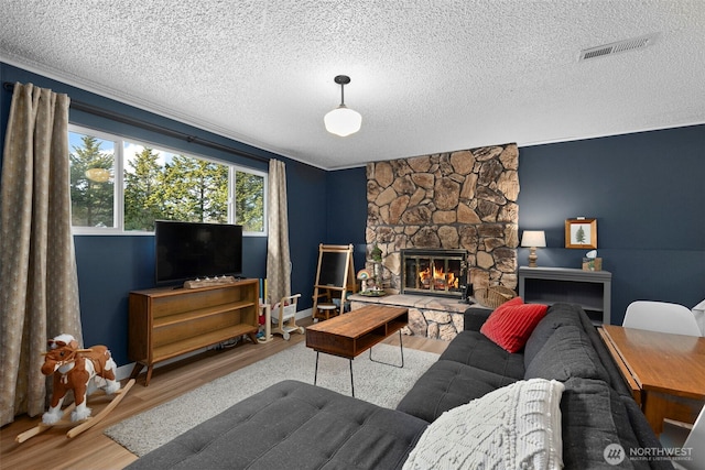 living room with visible vents, a fireplace, a textured ceiling, and wood finished floors