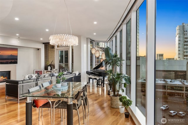 dining space featuring light wood-style floors, a lit fireplace, a wall of windows, and recessed lighting