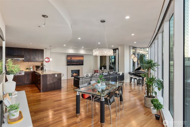 dining space with light wood finished floors, a warm lit fireplace, and recessed lighting